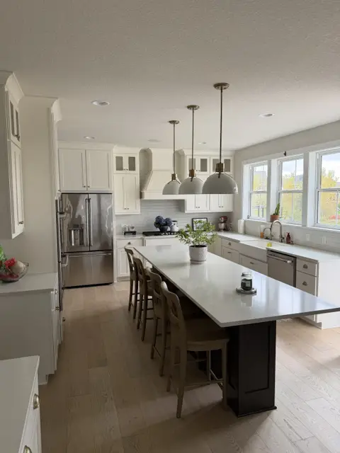 Clean open kitchen with a long white island, stainless refrigerator, white cabinets and pendant lights