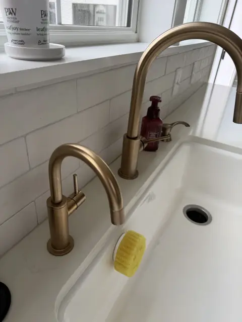 Clean white kitchen sink with a polished brass faucet and white tile backsplash