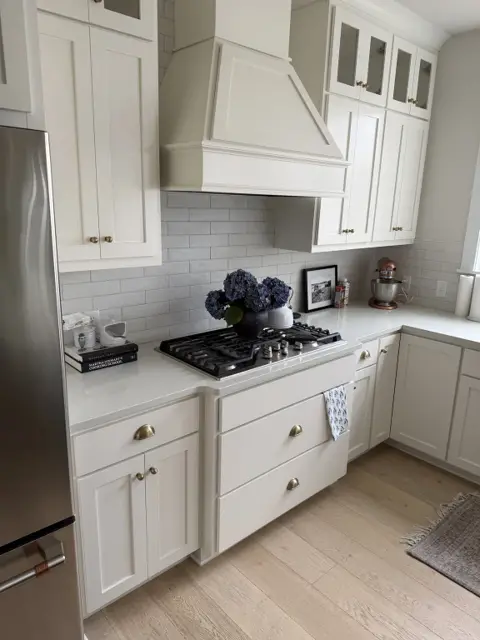 Cleaned gas stovetop, white quartz countertops and white cabinetry with range hood